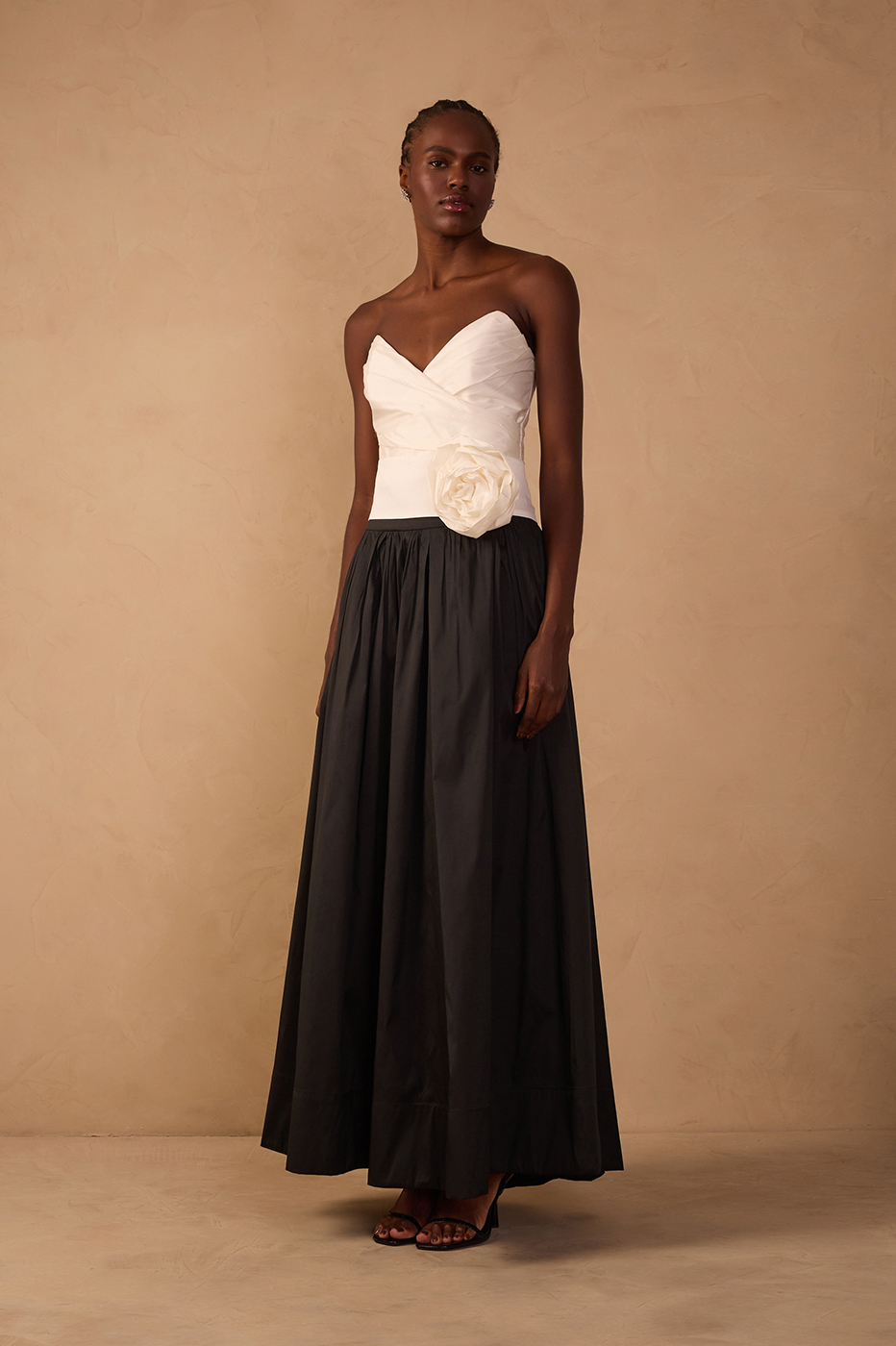 Woman wearing a white strapless top with rosette detail and a black flowing maxi skirt