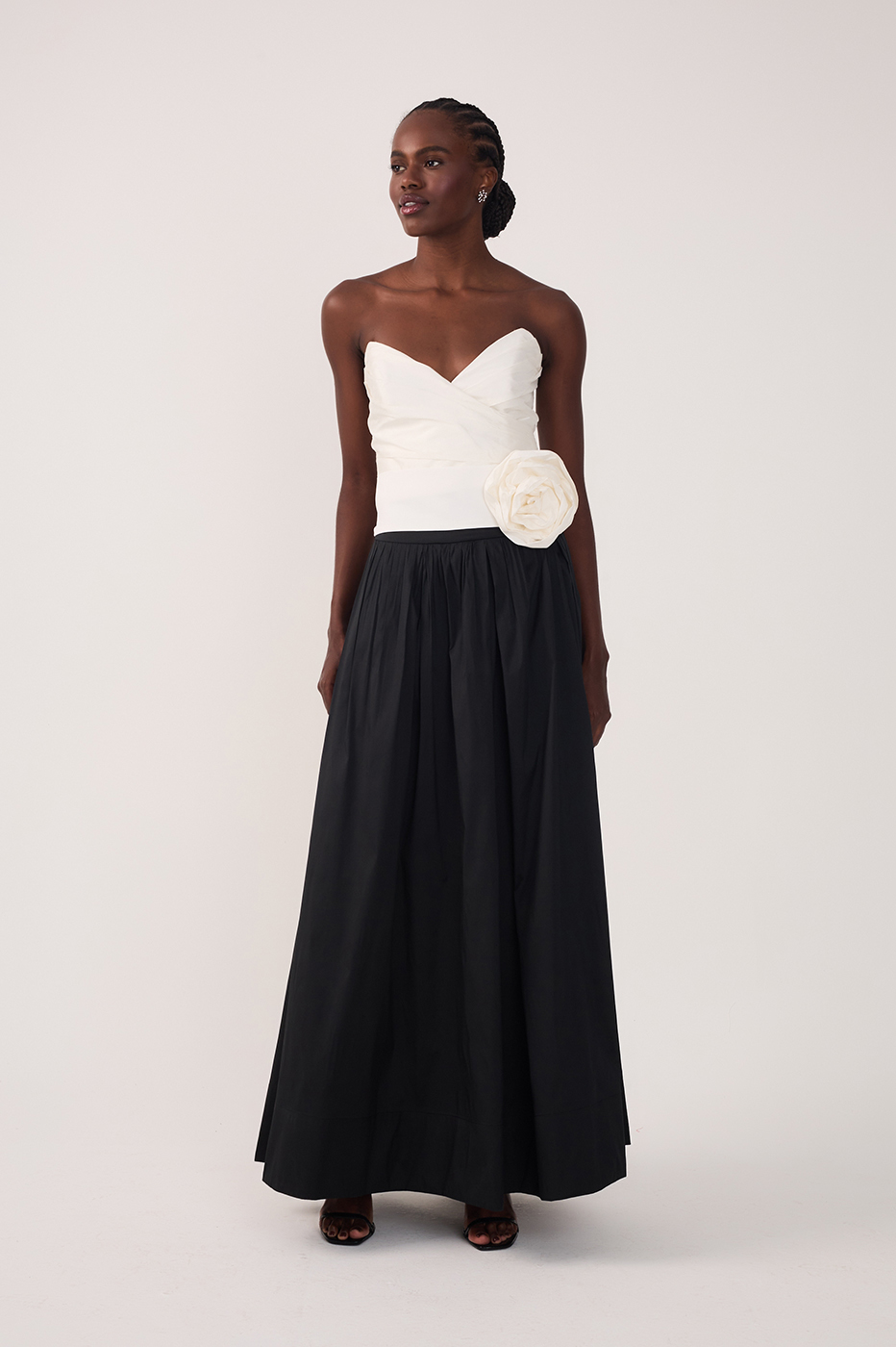 Front view of woman in white strapless rosette top and black high-waisted maxi skirt on light background