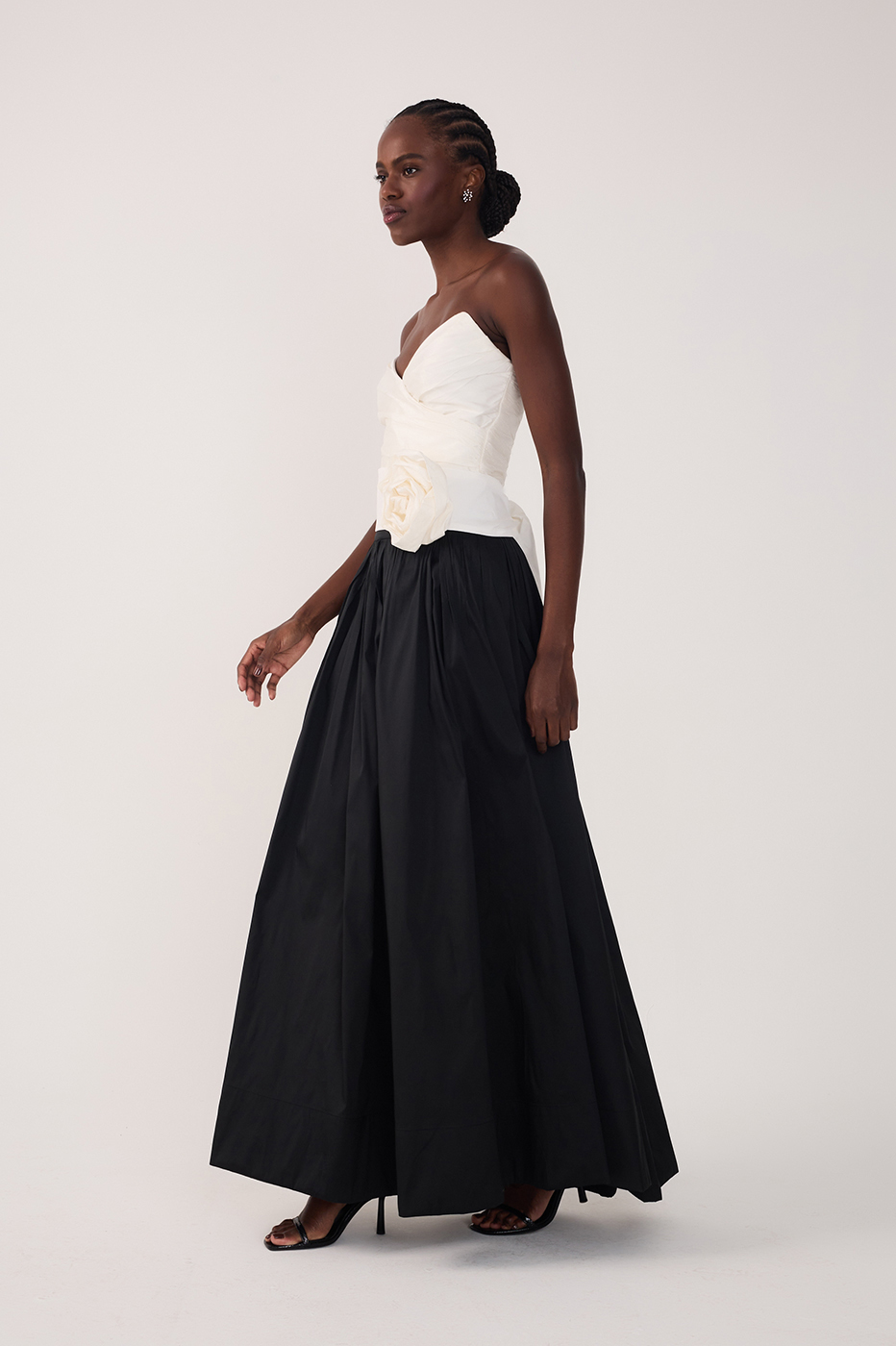 Side view of woman wearing a white strapless rosette top and a black full maxi skirt with heels