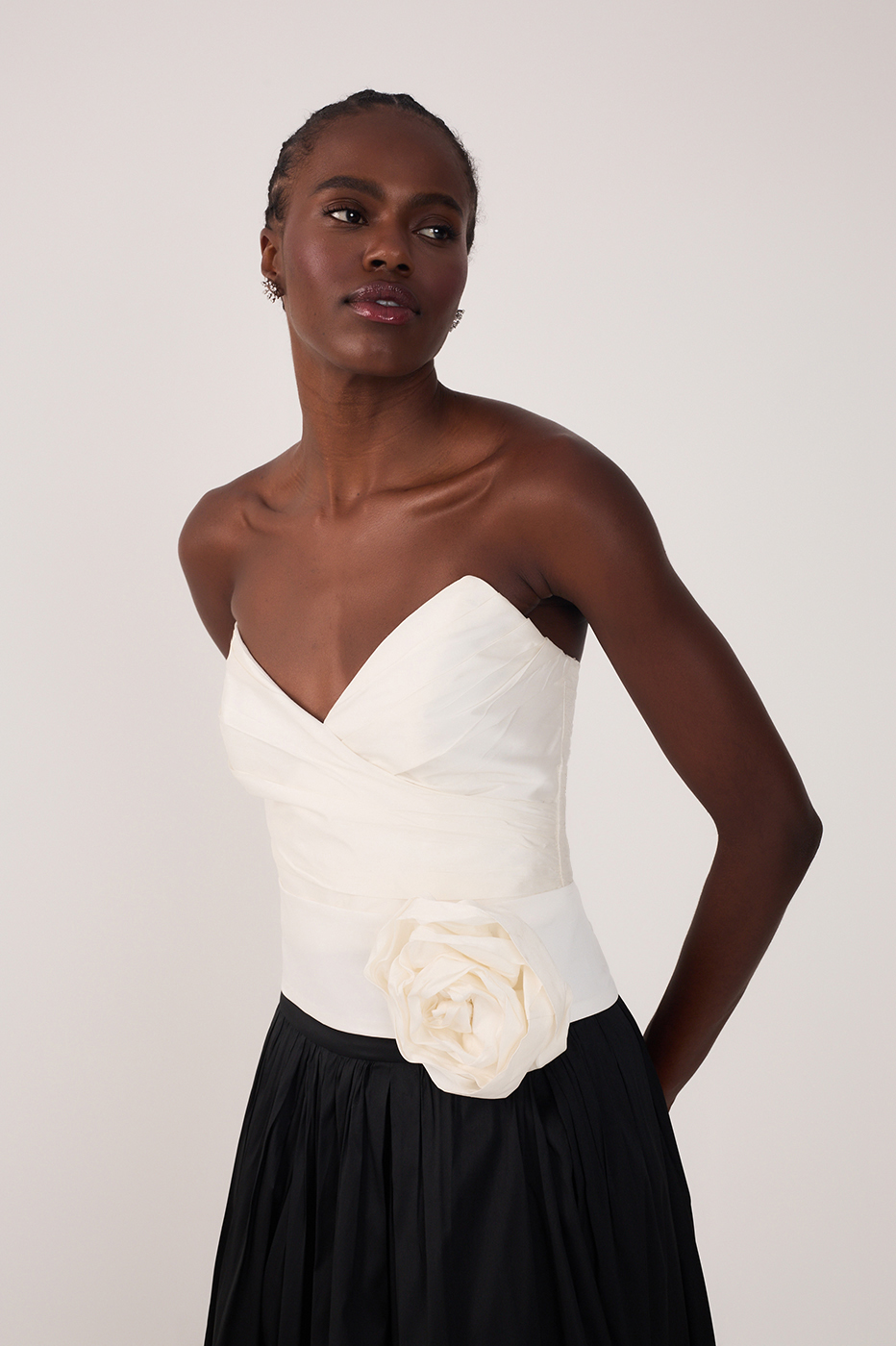 Woman posing in a white strapless draped top with rosette appliqué and black skirt