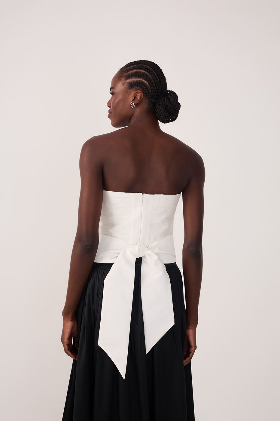 Back view of white strapless top with long bow tie detail worn with a black maxi skirt