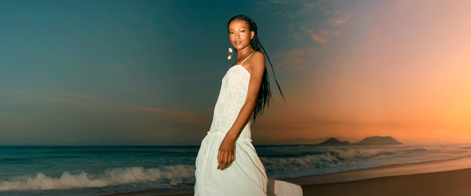 Woman in a white dress standing on a beach at sunset