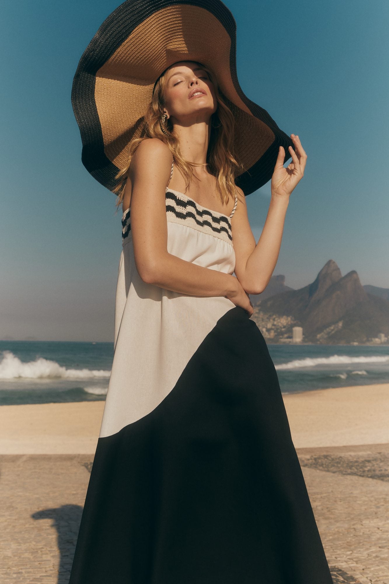 A woman in a wide straw hat and a black and white knit dress by the sea in Rio