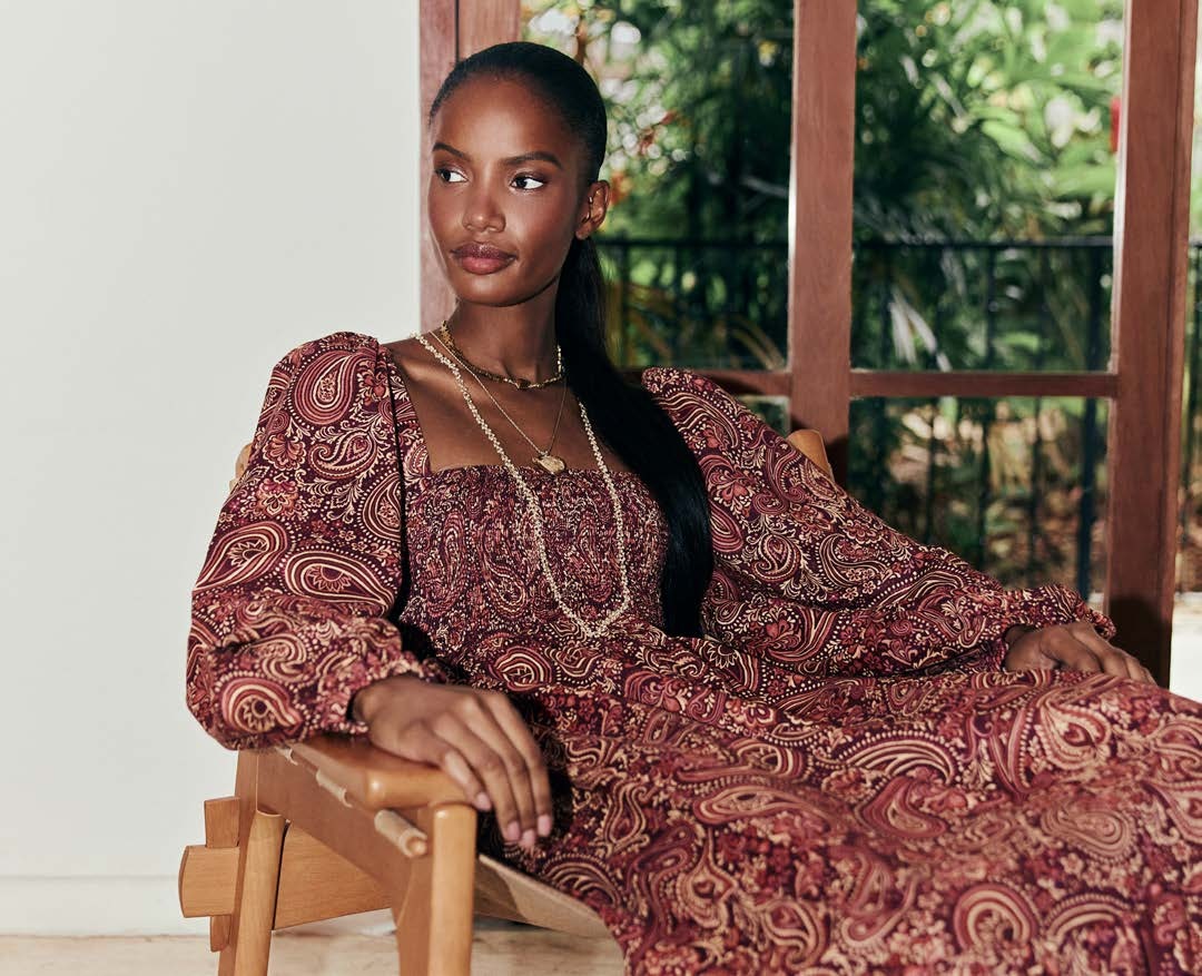 A woman in a paisley dress seated in a Rio de Janeiro house with a tropical garden behind