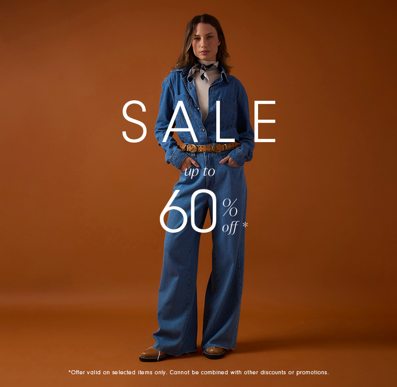 Vertical banner with a warm brown background. A woman stands centered wearing a denim shirt tucked into wide-leg denim pants, styled with a brown belt, light top underneath, neck scarf, and flat shoes. Overlaid text reads “SALE,” below it “up to 60% off*.” At the bottom, small text says “*Offer valid on selected items only. Cannot be combined with other discounts or promotions.”