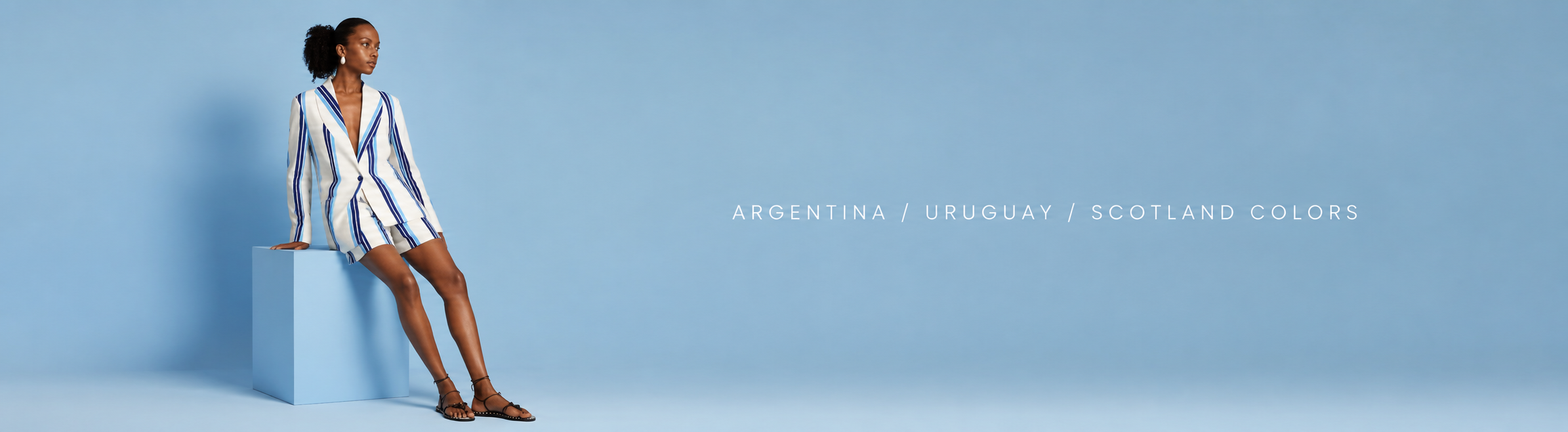 Woman wearing a blue and white striped blazer dress sitting on a light blue cube against a light blue background, with the text "Argentina / Uruguay / Scotland Colors"