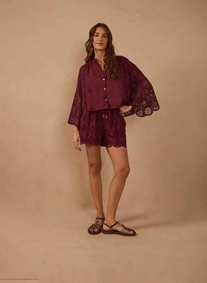 Matching sets category banner: model against a beige backdrop wearing a burgundy eyelet lace blouse and matching shorts with leather sandals