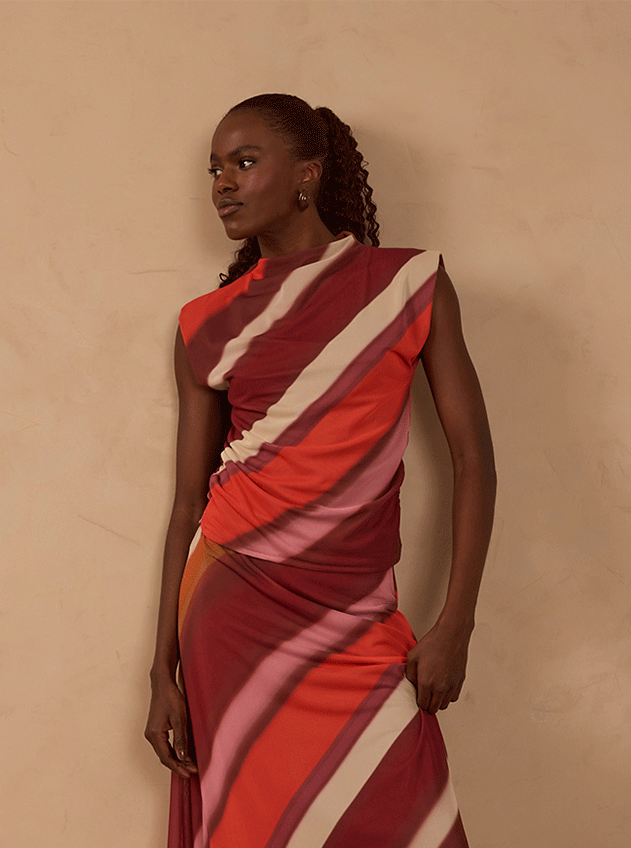 Shop by size L banner: woman in a draped sleeveless dress with diagonal red, pink and cream stripes against a beige backdrop
