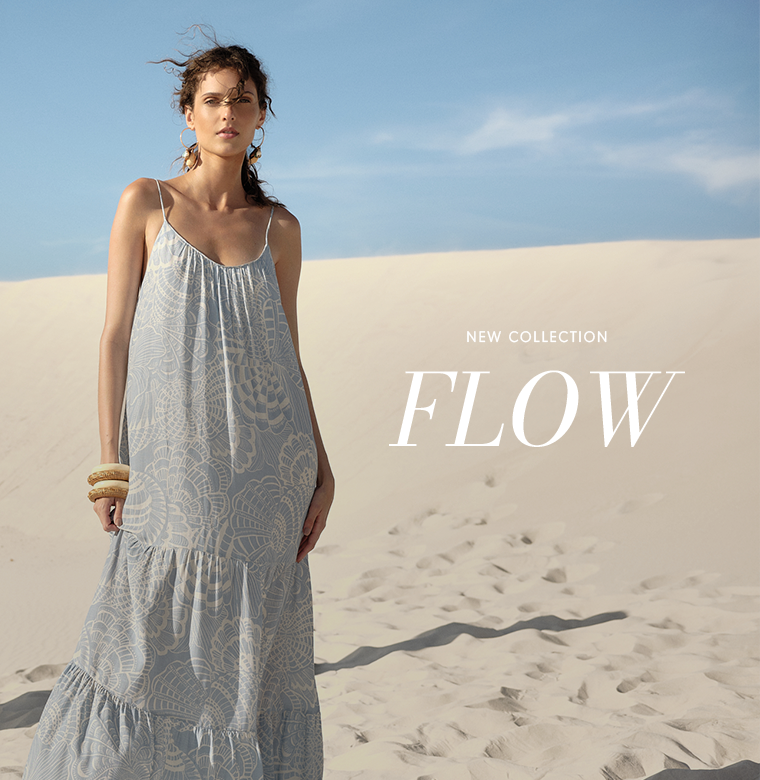 "New Collection FLOW" banner featuring a woman in a long light blue patterned maxi dress with hoop earrings, standing on sand dunes.