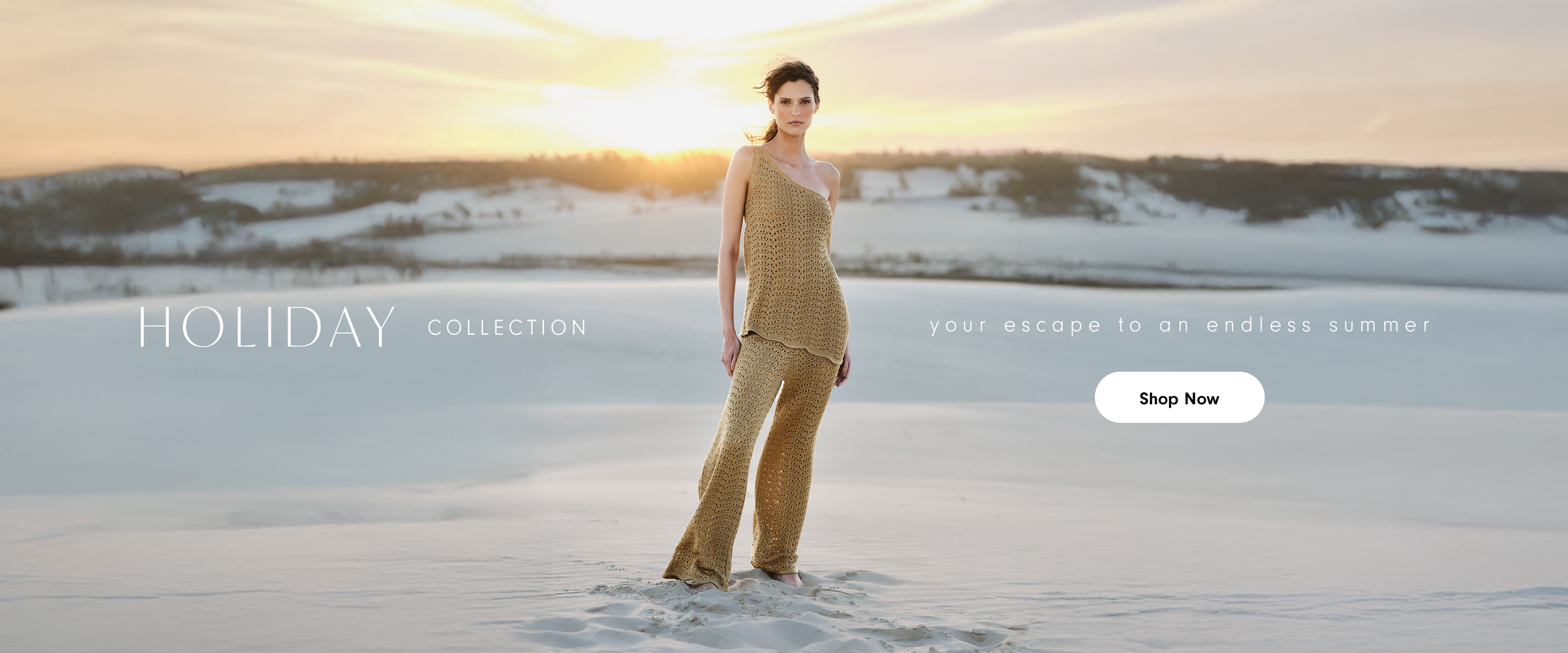 Dress To Holiday Collection banner featuring model wearing gold beige crochet knit crop top and wide-leg pants set, standing barefoot on white sandy beach with ocean and sunset sky in background. Warm golden hour lighting creates dreamy vacation atmosphere. Text reads 'HOLIDAY COLLECTION - your escape to an endless summer' with Shop Now button. Sustainable resort wear and beachwear for tropical getaways.