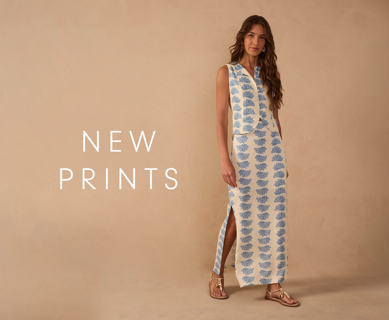 "New Prints" banner featuring a woman in a blue and white seashell printed vest and long skirt set with sandals.