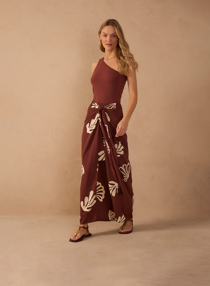 Woman wearing a one-shoulder brown bodysuit with a brown floral-print wrap sarong skirt and gold sandals
