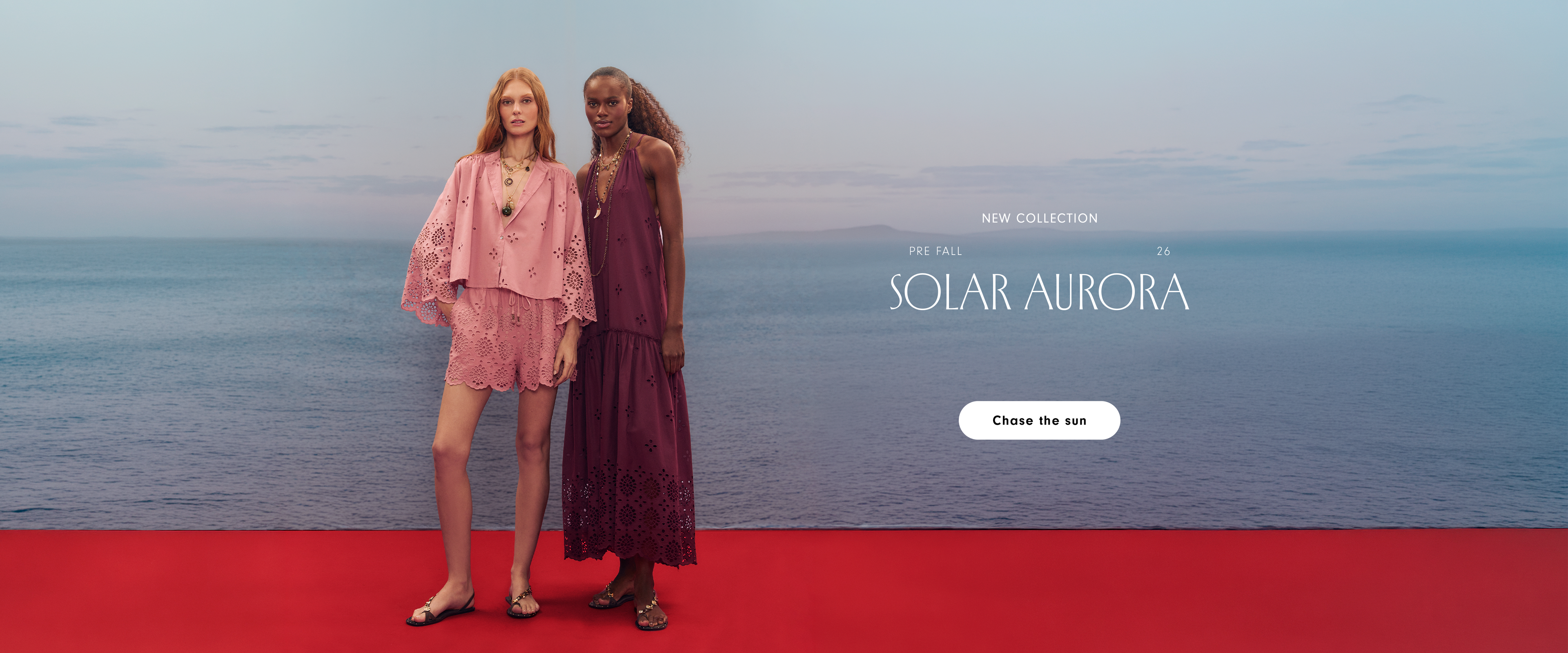 Pre Fall 26 Solar Aurora new collection desktop banner: two women by the sea on a red platform, one in a pink eyelet set and one in a burgundy dress, with a Chase the sun button