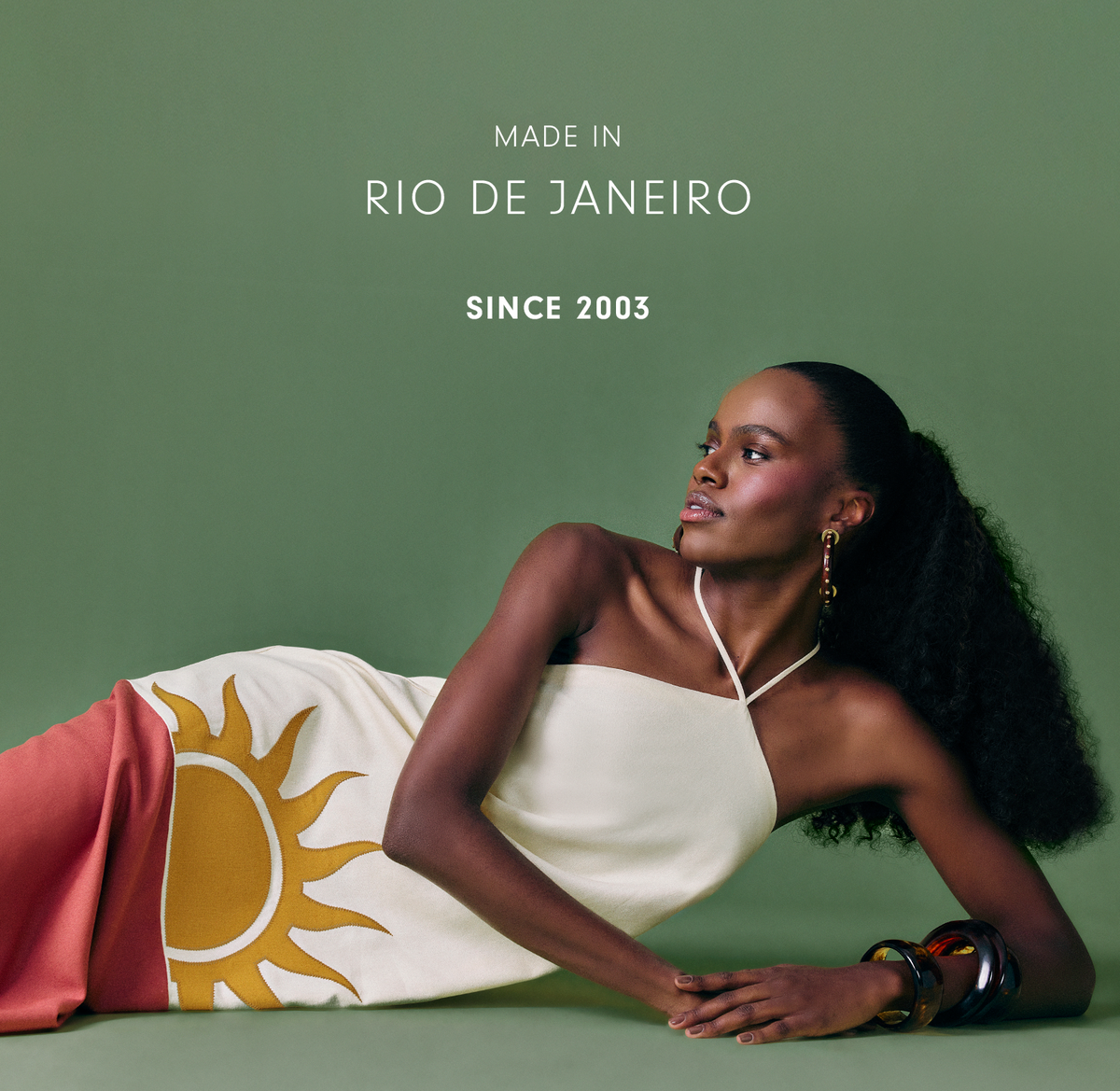 "Made in Rio de Janeiro since 2003" mobile banner: model lying on a green backdrop wearing a cream halter dress with a yellow sun print