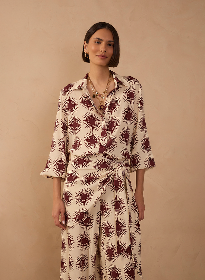 Woman in a cream and burgundy sunburst print shirt and matching wrap skirt with layered gold necklaces