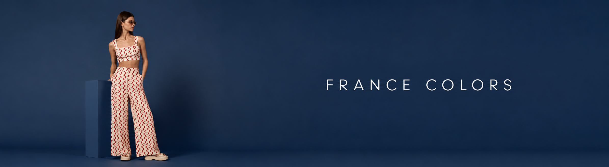 Woman wearing a printed crop top and matching wide-leg pants standing against a blue wall, with the text "France Colors"