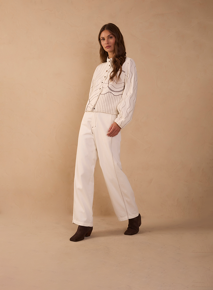 Woman in an off-white embroidered blouse with wide-leg cream trousers and brown ankle boots