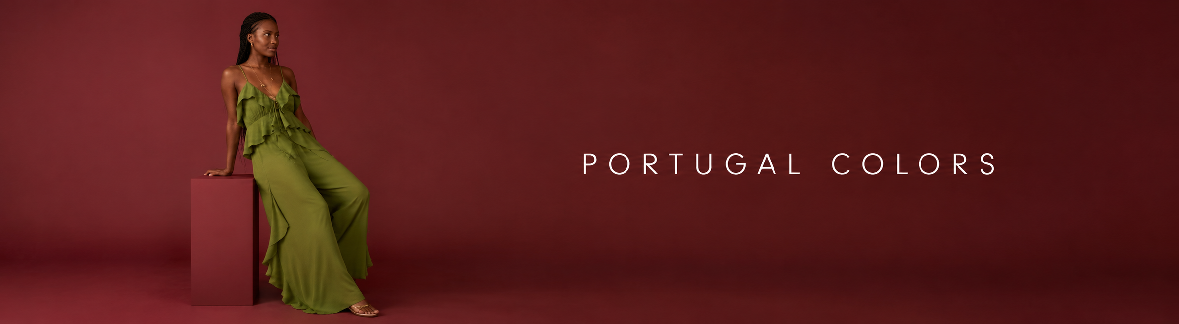 Woman in a green ruffled top and wide-leg green trousers seated against a deep red background; banner reading Portugal colors