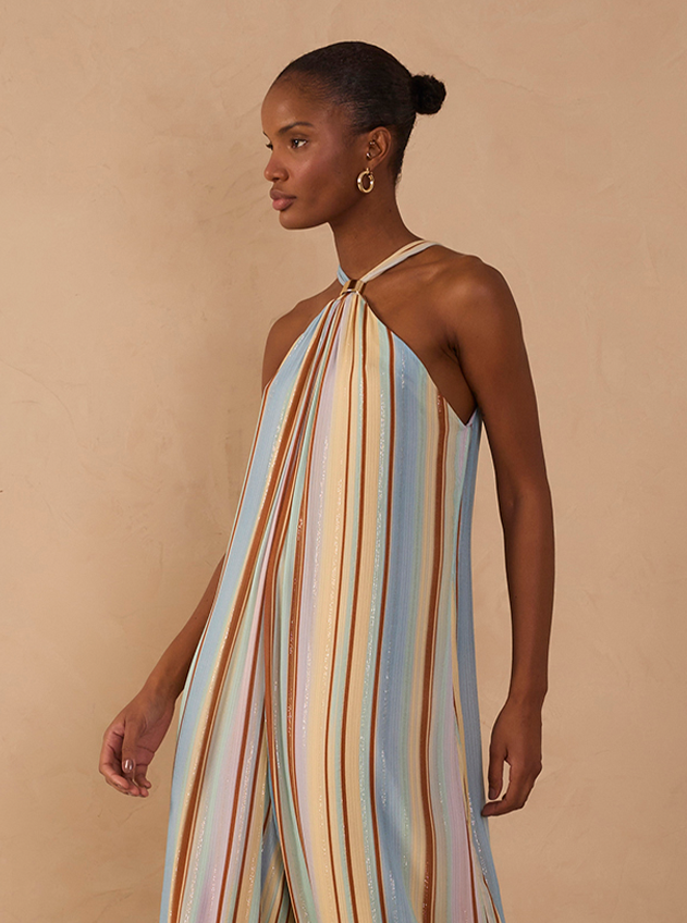 Woman wearing a multicolored striped halter neck jumpsuit with gold hoop earrings.