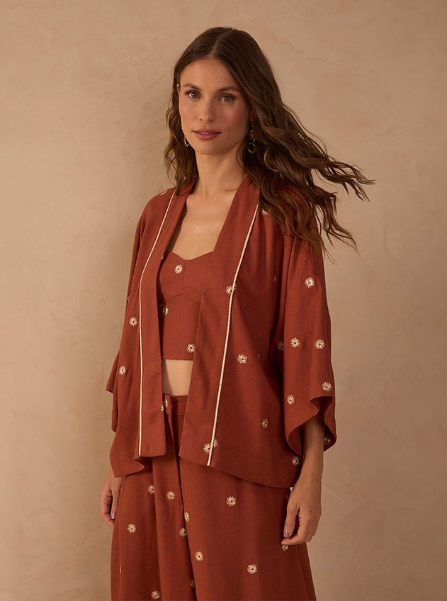 Woman in a rust terracotta embroidered floral set with a kimono jacket, cropped bralette and wide-leg trousers