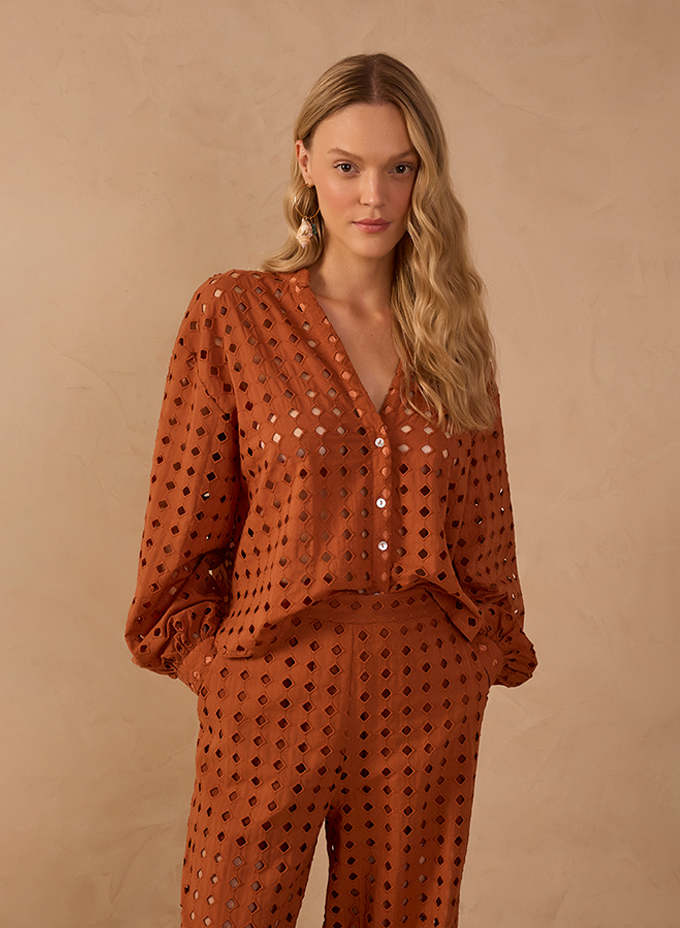 Woman wearing a rust-colored eyelet cutout button-up blouse and matching wide-leg pants against a beige backdrop