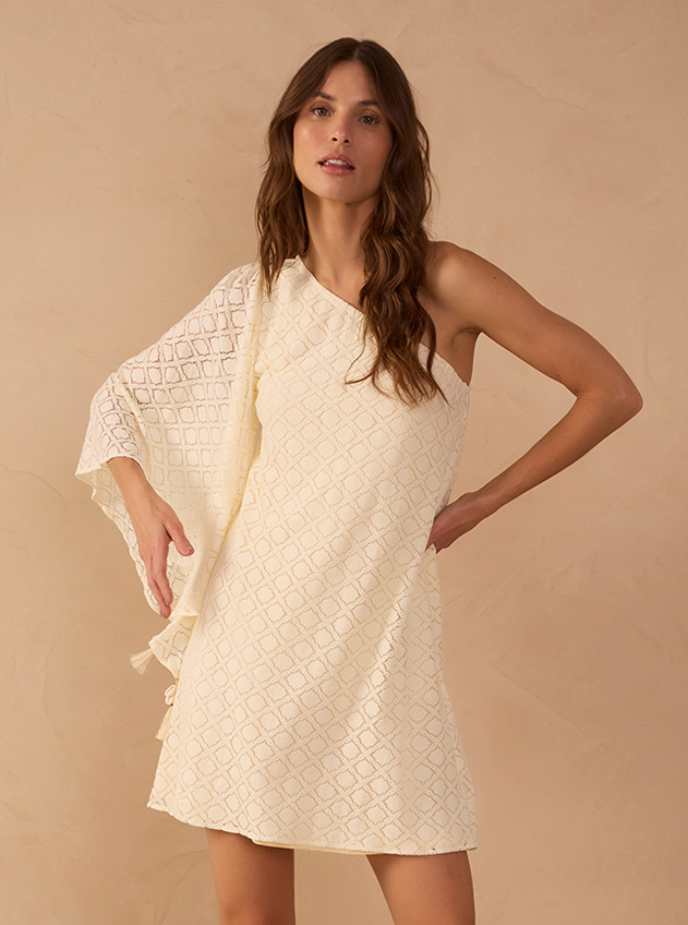 Woman wearing an ivory one-shoulder mini dress with geometric textured pattern and flared sleeve