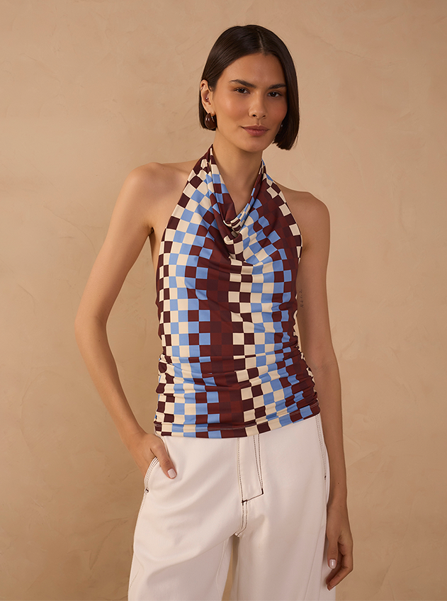 Woman with a dark bob wearing a brown, blue and cream checkerboard halter neck top and cream wide-leg trousers