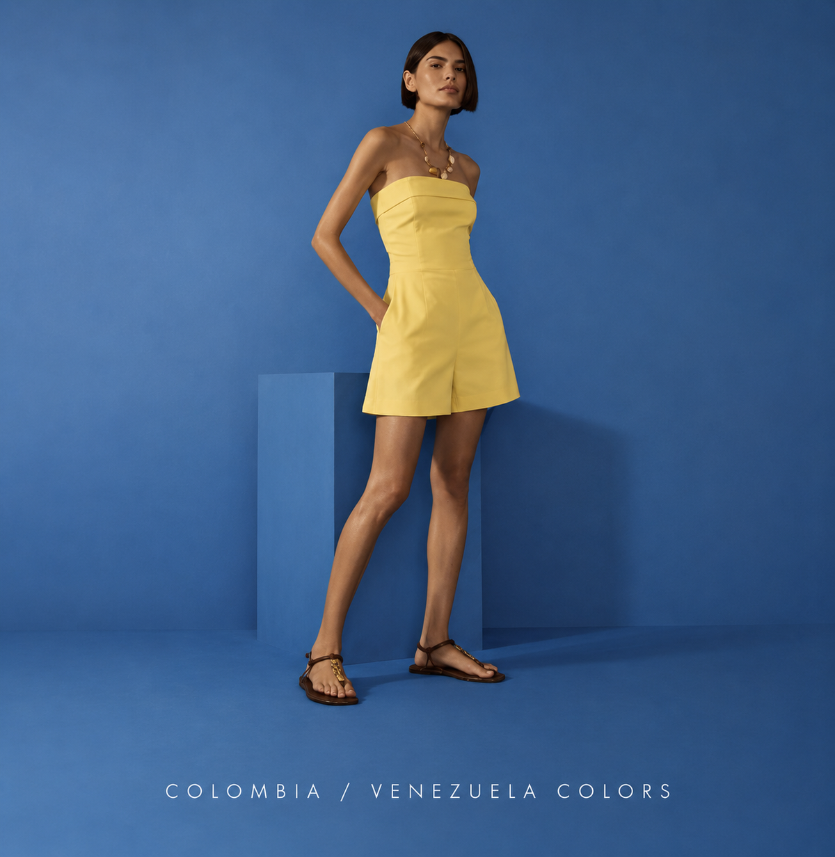 Woman wearing a yellow strapless romper standing against a blue studio background with sandals, captioned Colombia / Venezuela Colors