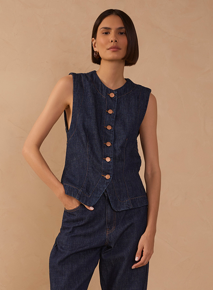 Model wearing a sleeveless dark denim button-front vest with matching wide-leg jeans against a beige backdrop